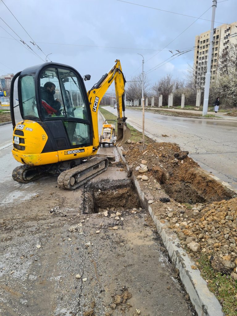 Мини багер по тротоара — единственото, което се побира между дърветата и оградата.