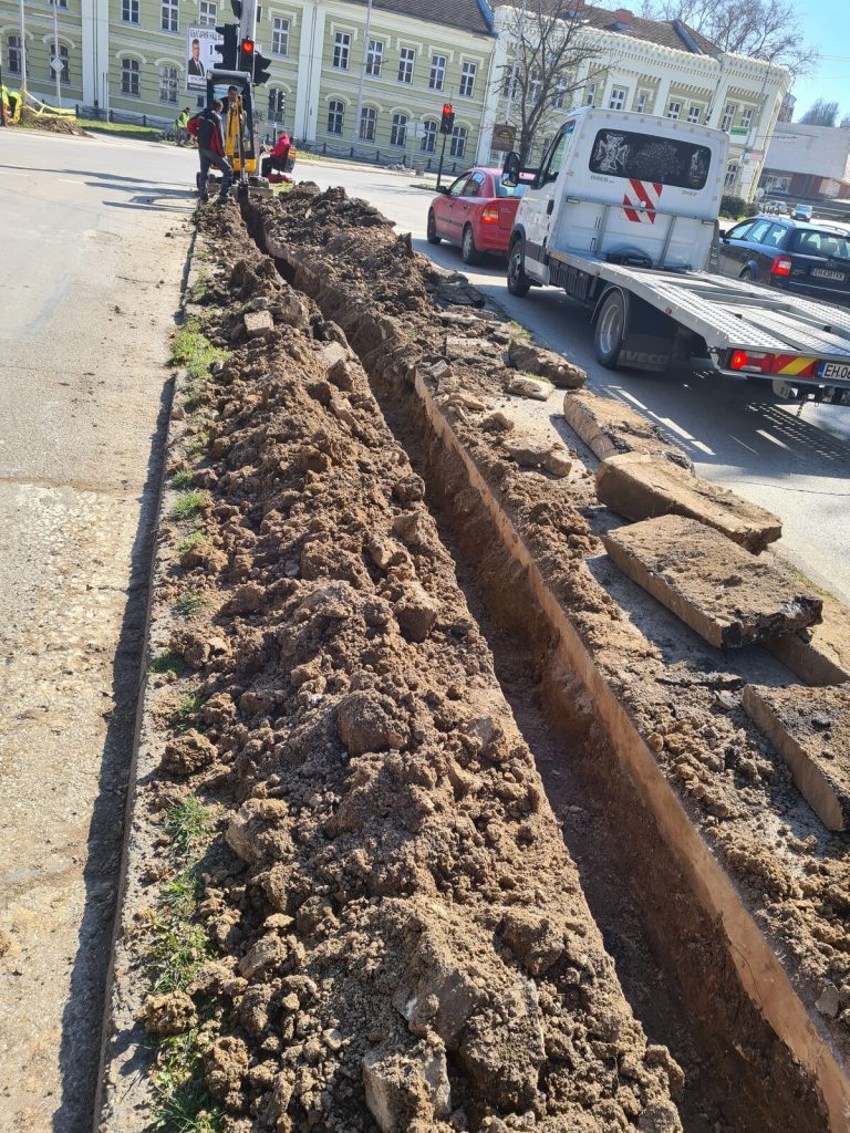 Отворен изкоп с положени тръби по дължината на тротоара.
